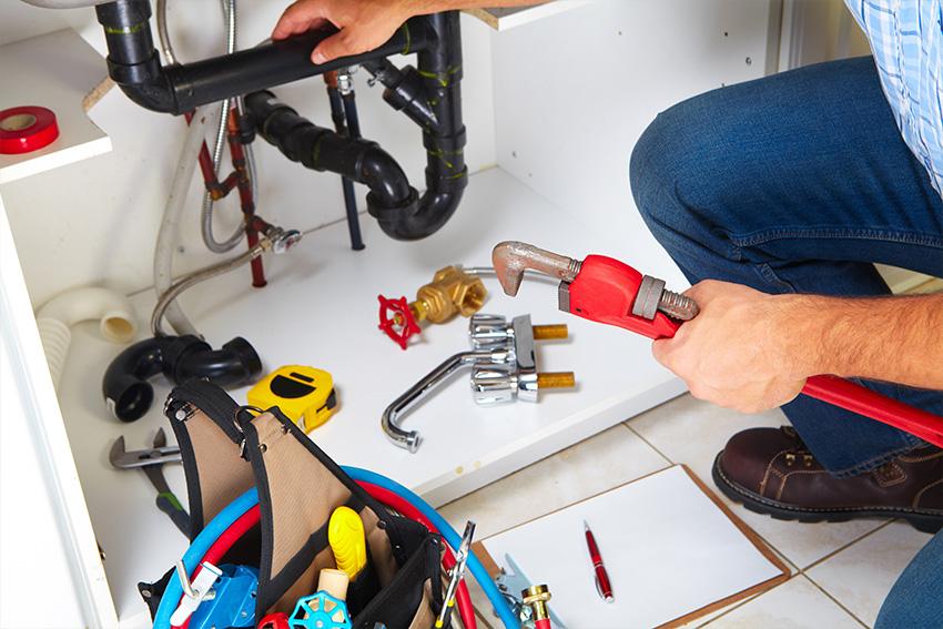 Rohrreinigung Treptow – Klempner kniet sich neben seinem Werkzeug vor einem Spülenschrank hin